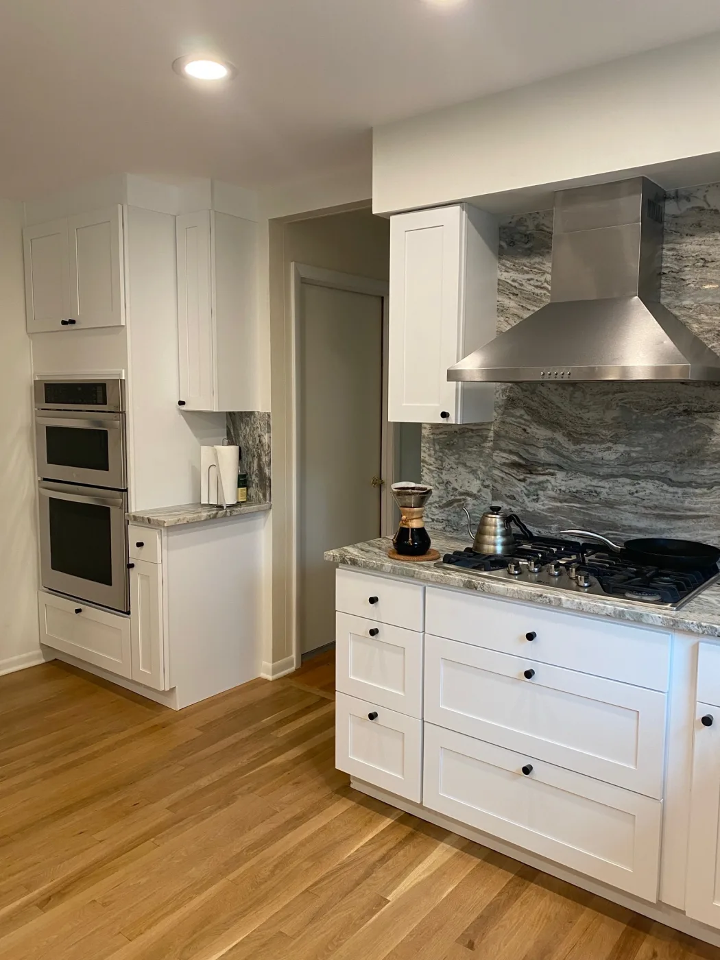 White shaker kitchen with wall ovens and a stainless cooktop hood